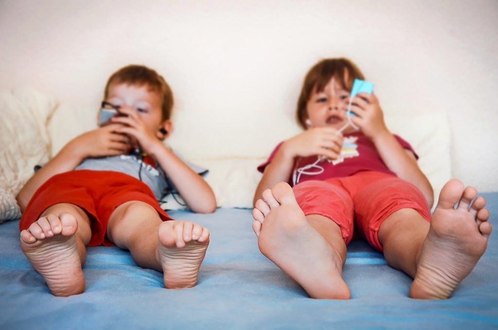 Small children relaxing with their mobile devices. Kids being kids, digital entertaining at home.