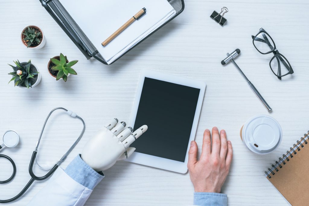 cropped image of male doctor with prosthetic arm using digital tablet with blank screen at table
