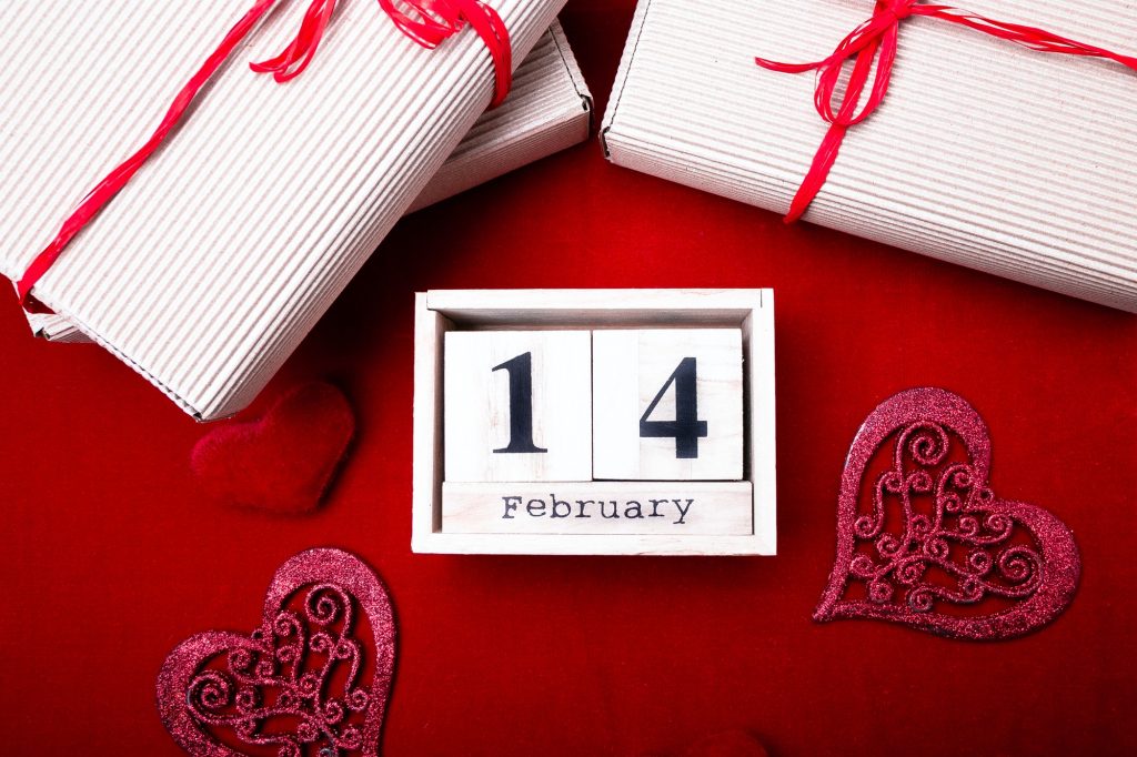 Wooden calendar show of February 14 with red heart and gift boxes.