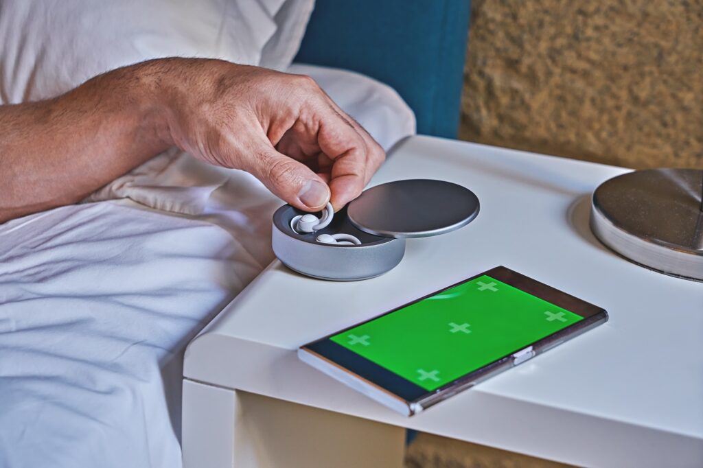 Man takes one of noise-masking sleep buds from holder on table.