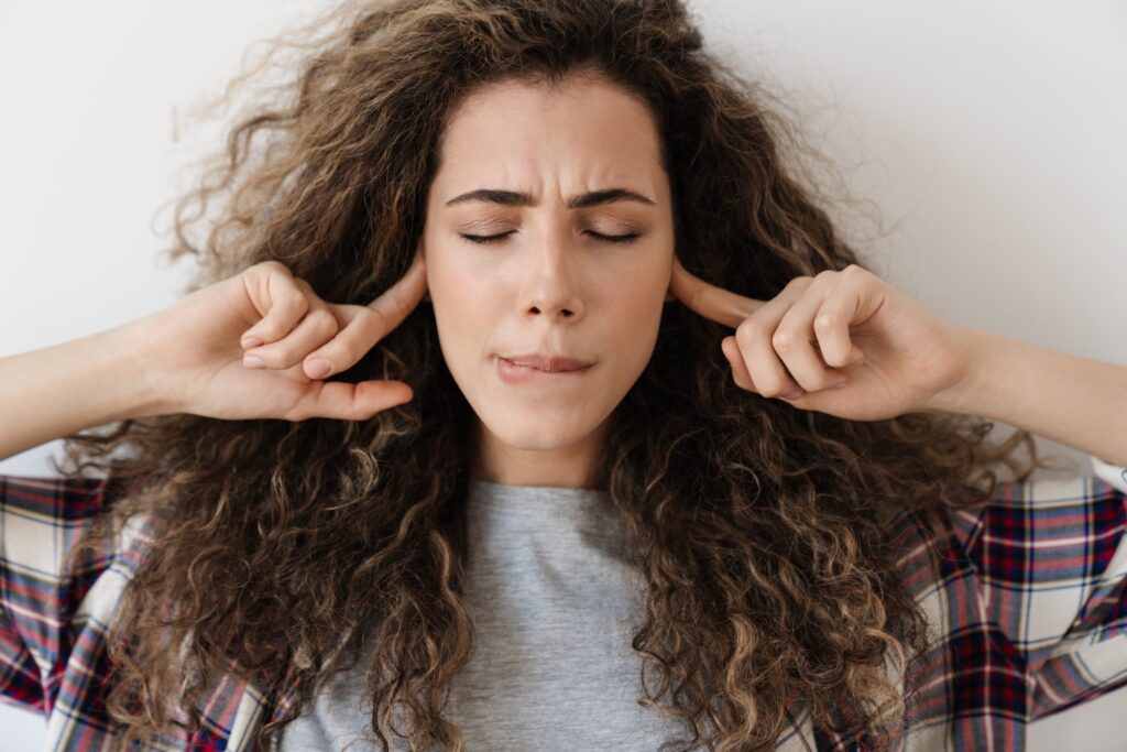 Photo of displeased woman plugging her ears while posing on camera