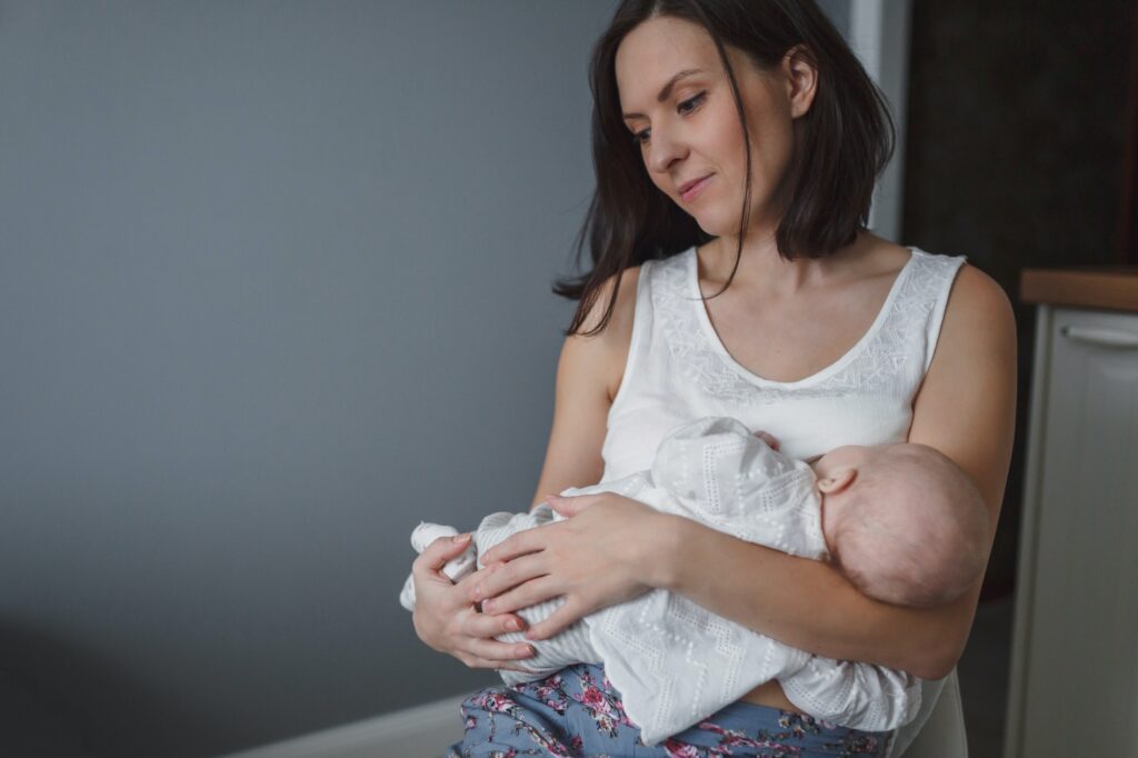 Young beautiful woman is breastfeeding a little baby in a cozy room