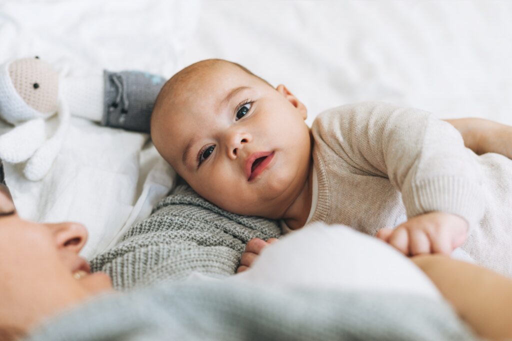 Young mom with cute baby boy, mother breast-feeds baby on bed