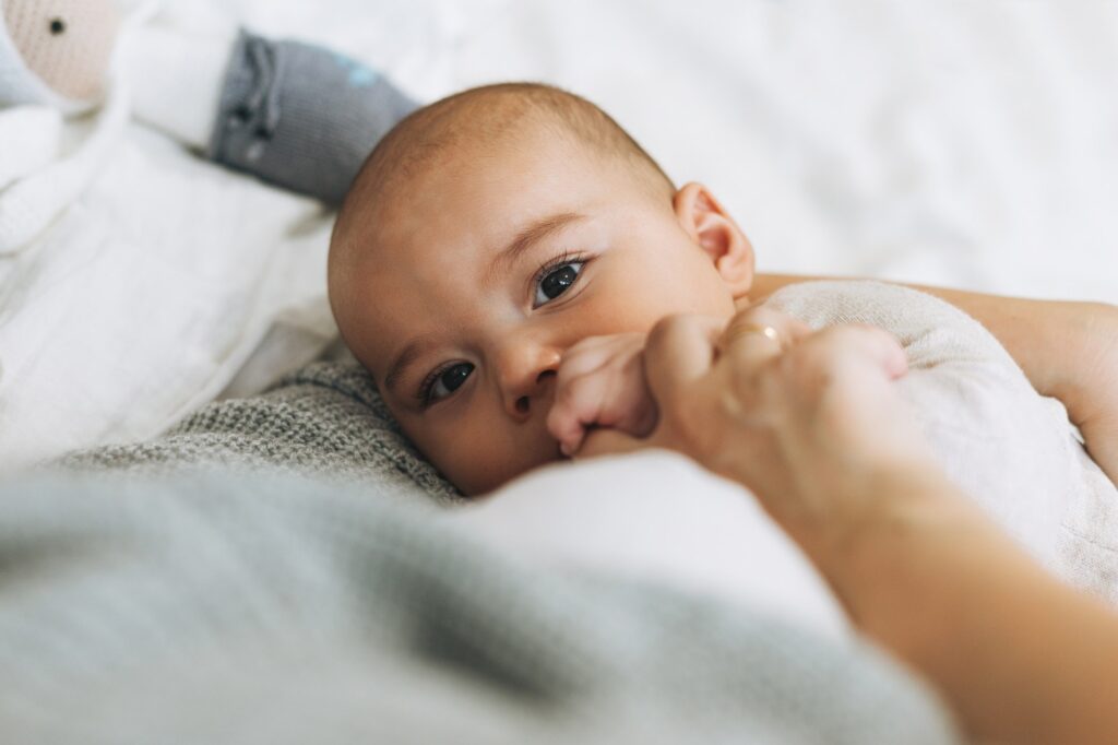 Young mom with cute baby boy, mother breast-feeds baby on bed
