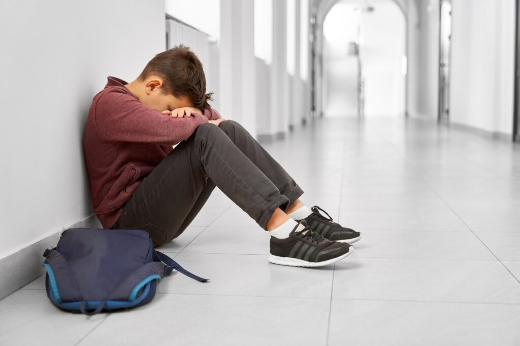Sad school boy sitting alone on floor at corridor